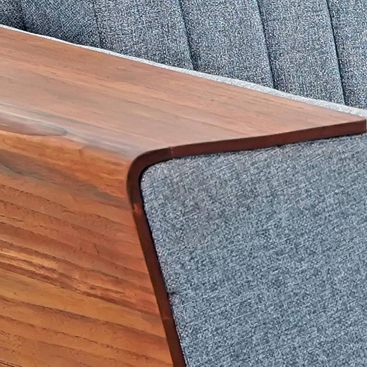 Introducing the Wooden Wing Sofa by Tooba Furniture Factory, a sleek and modern piece featuring light gray cushioning and distinctive wooden side panels. The vertically tufted backrest provides a touch of elegance, while the sofa is supported by angled wooden legs. The wide, flat armrests are crafted from the same wood as the side panels, seamlessly combining style and comfort.