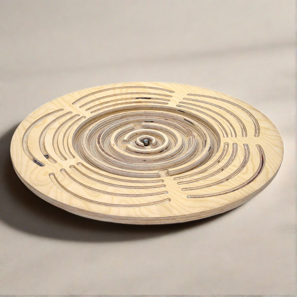 Introducing the Circular Labyrinth Balance Board by Tooba Furniture Factory: a meticulously crafted round wooden game featuring concentric paths and intricate passages carved into its surface. It includes a small metal ball that players must navigate through the maze by tilting and maneuvering, much like a delicate balance board.