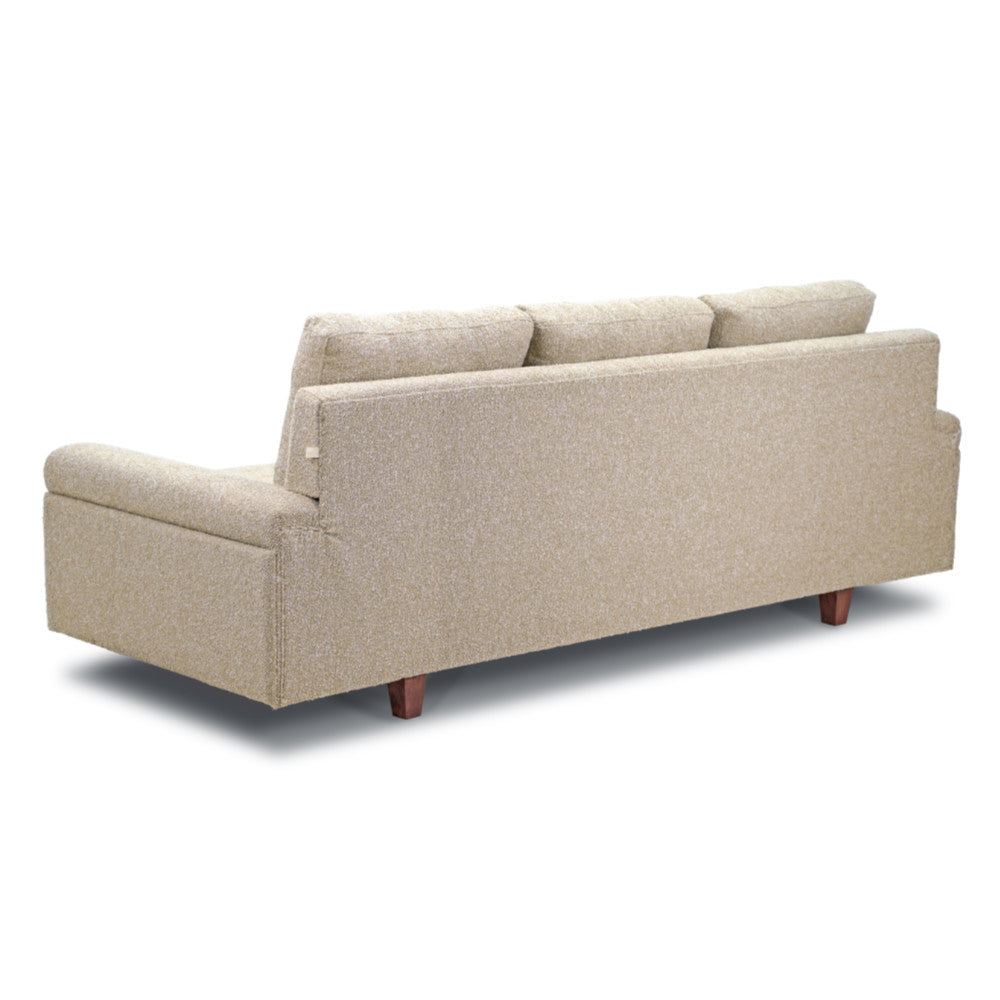 A light beige Meta Boucle sofa from Tooba Furniture Factory, featuring three back cushions, is displayed against a white background. This three-seater sofa boasts a modern design with plush upholstery and slightly angled armrests. It rests on four short, dark wooden legs.