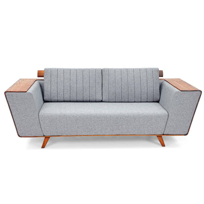 Introducing the Wooden Wing Sofa by Tooba Furniture Factory, a sleek and modern piece featuring light gray cushioning and distinctive wooden side panels. The vertically tufted backrest provides a touch of elegance, while the sofa is supported by angled wooden legs. The wide, flat armrests are crafted from the same wood as the side panels, seamlessly combining style and comfort.