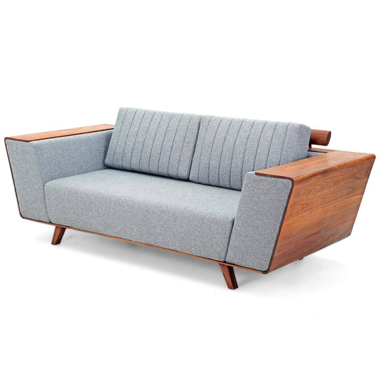 Introducing the Wooden Wing Sofa by Tooba Furniture Factory, a sleek and modern piece featuring light gray cushioning and distinctive wooden side panels. The vertically tufted backrest provides a touch of elegance, while the sofa is supported by angled wooden legs. The wide, flat armrests are crafted from the same wood as the side panels, seamlessly combining style and comfort.