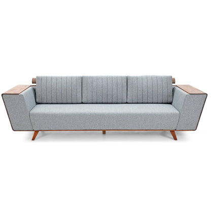 Introducing the Wooden Wing Sofa by Tooba Furniture Factory, a sleek and modern piece featuring light gray cushioning and distinctive wooden side panels. The vertically tufted backrest provides a touch of elegance, while the sofa is supported by angled wooden legs. The wide, flat armrests are crafted from the same wood as the side panels, seamlessly combining style and comfort.