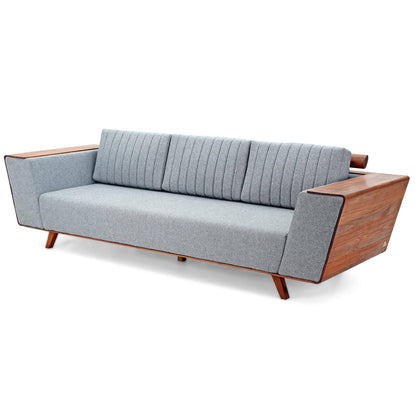 Introducing the Wooden Wing Sofa by Tooba Furniture Factory, a sleek and modern piece featuring light gray cushioning and distinctive wooden side panels. The vertically tufted backrest provides a touch of elegance, while the sofa is supported by angled wooden legs. The wide, flat armrests are crafted from the same wood as the side panels, seamlessly combining style and comfort.