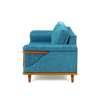 The Quantum Sofa by Tooba Furniture Factory is a modern teal upholstered piece that boasts a wooden frame and legs. It features simple, clean lines, cushioned armrests, and an angled backrest with a quilted design. Wooden accents enhance its stylish and contemporary appeal.