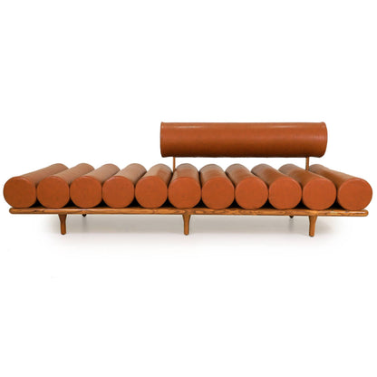 The Cylinder Cushion Sofa by Tooba Furniture Factory is a modern, minimalist piece with a distinct design featuring multiple cylindrical cushions arranged horizontally on a wooden frame. The cushions are upholstered in brown leather, and the backrest is made from a single, long cylindrical cushion.