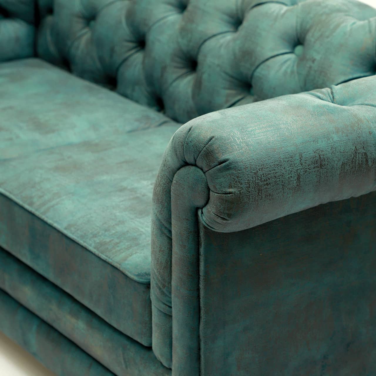 A teal, tufted velvet Chesterfield Sofa by Tooba Furniture Factory with rolled arms and back, featuring two seat cushions and standing on short wooden legs. The fabric appears plush and luxurious, with deep button detailing on the back and arms—truly a statement sofa exuding medieval elegance.